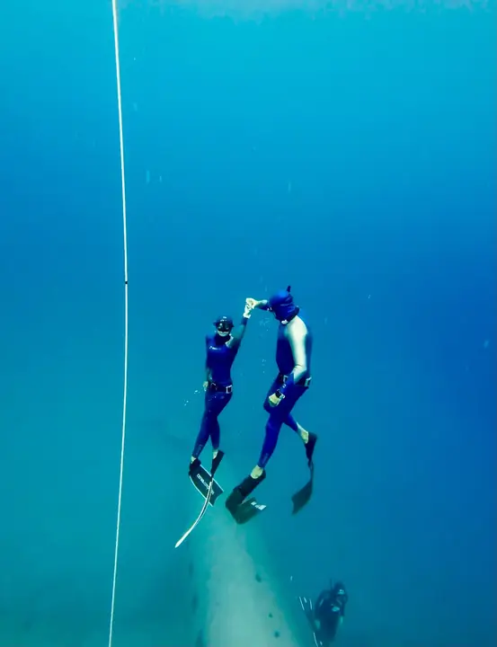 Two freedivers meeting underwater beside the dive line
